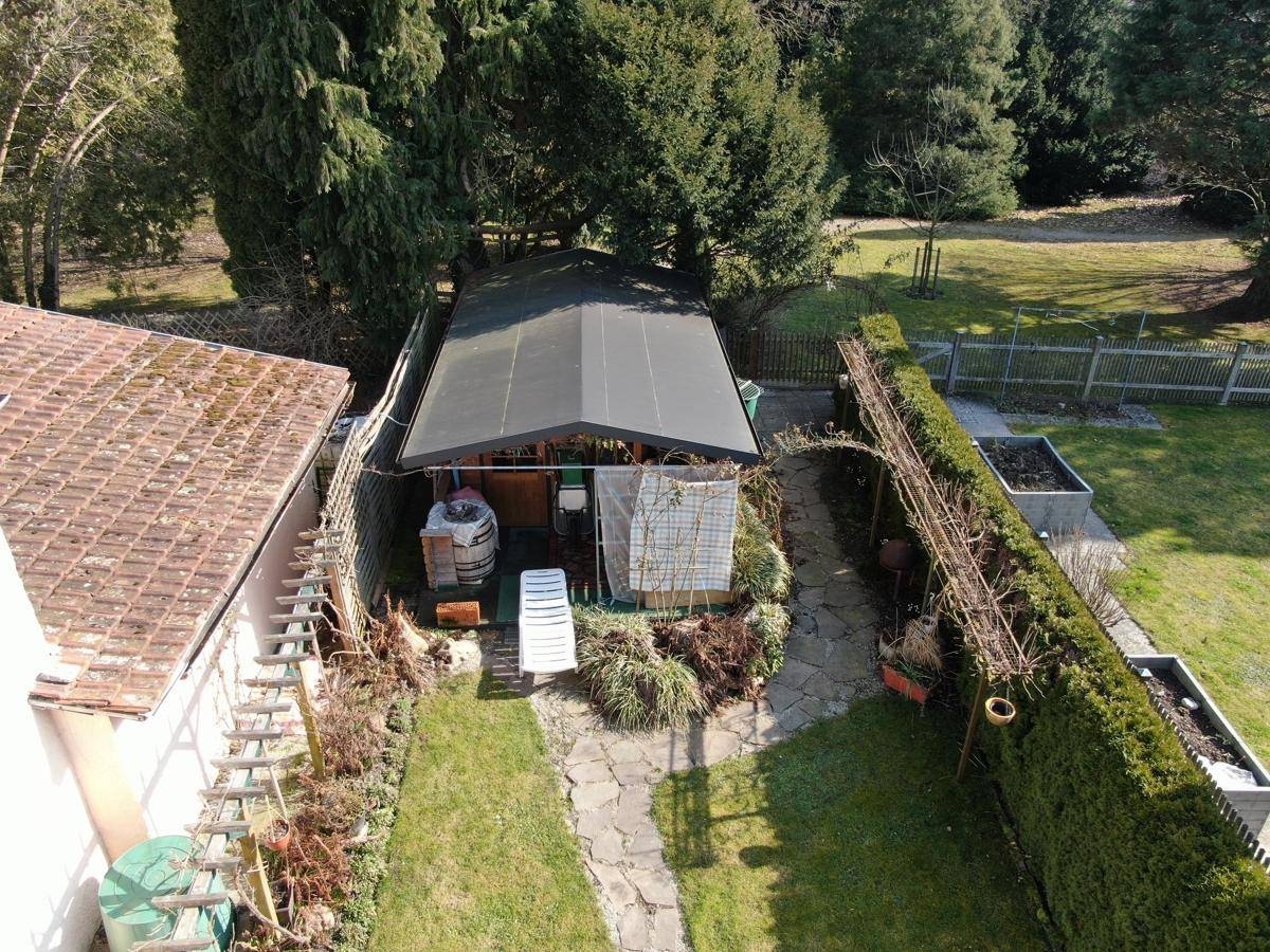 Luftaufnahme des Gartens mit Gartenhaus, Rasenfläche und umgebenden Bäumen.