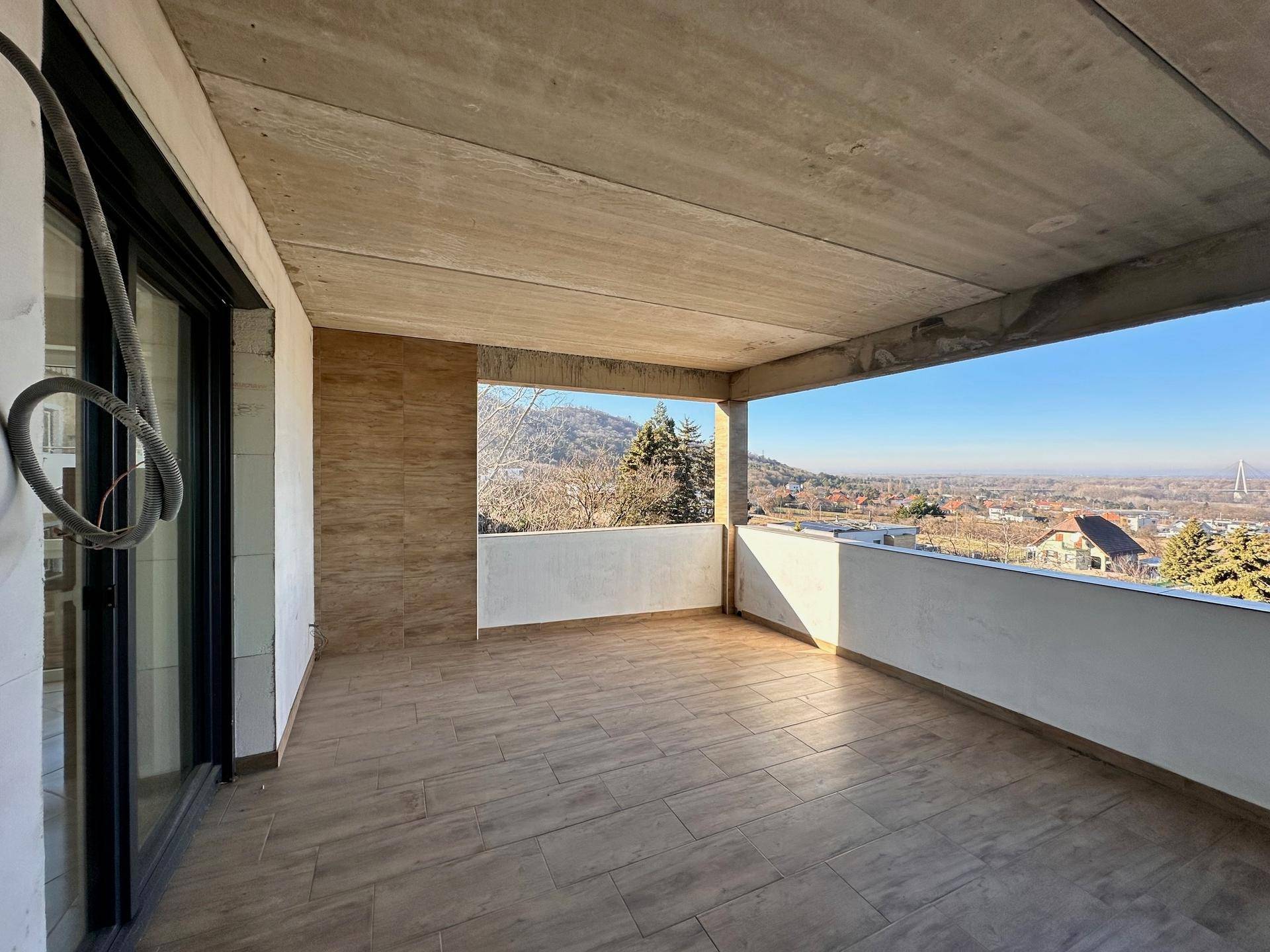 Großer überdachter Balkon mit Fliesenboden und weitem Blick über die Stadt und die Hügel.