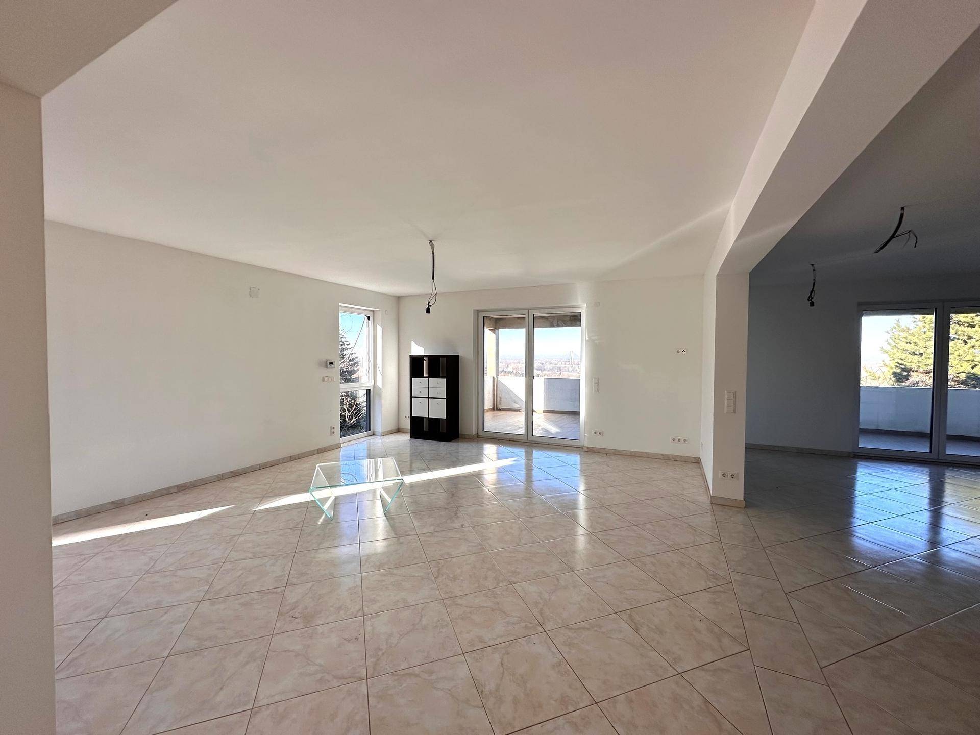 Heller, leerer Wohnbereich mit Fliesenboden, großen Fenstern und Zugang zu einem Balkon.