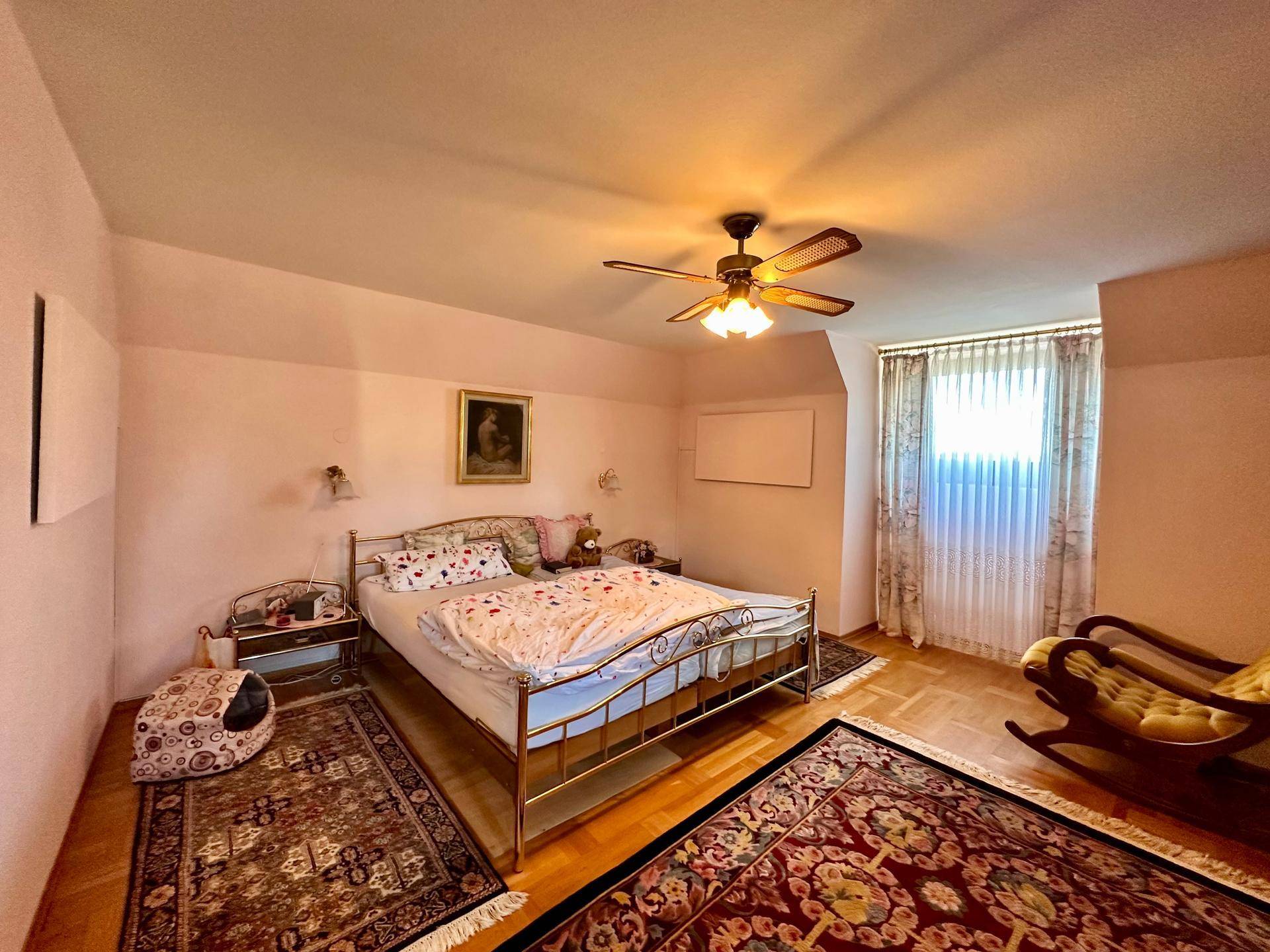 Geräumiges Schlafzimmer mit Doppelbett, Parkettboden und einem großen Fenster für viel Tageslicht.