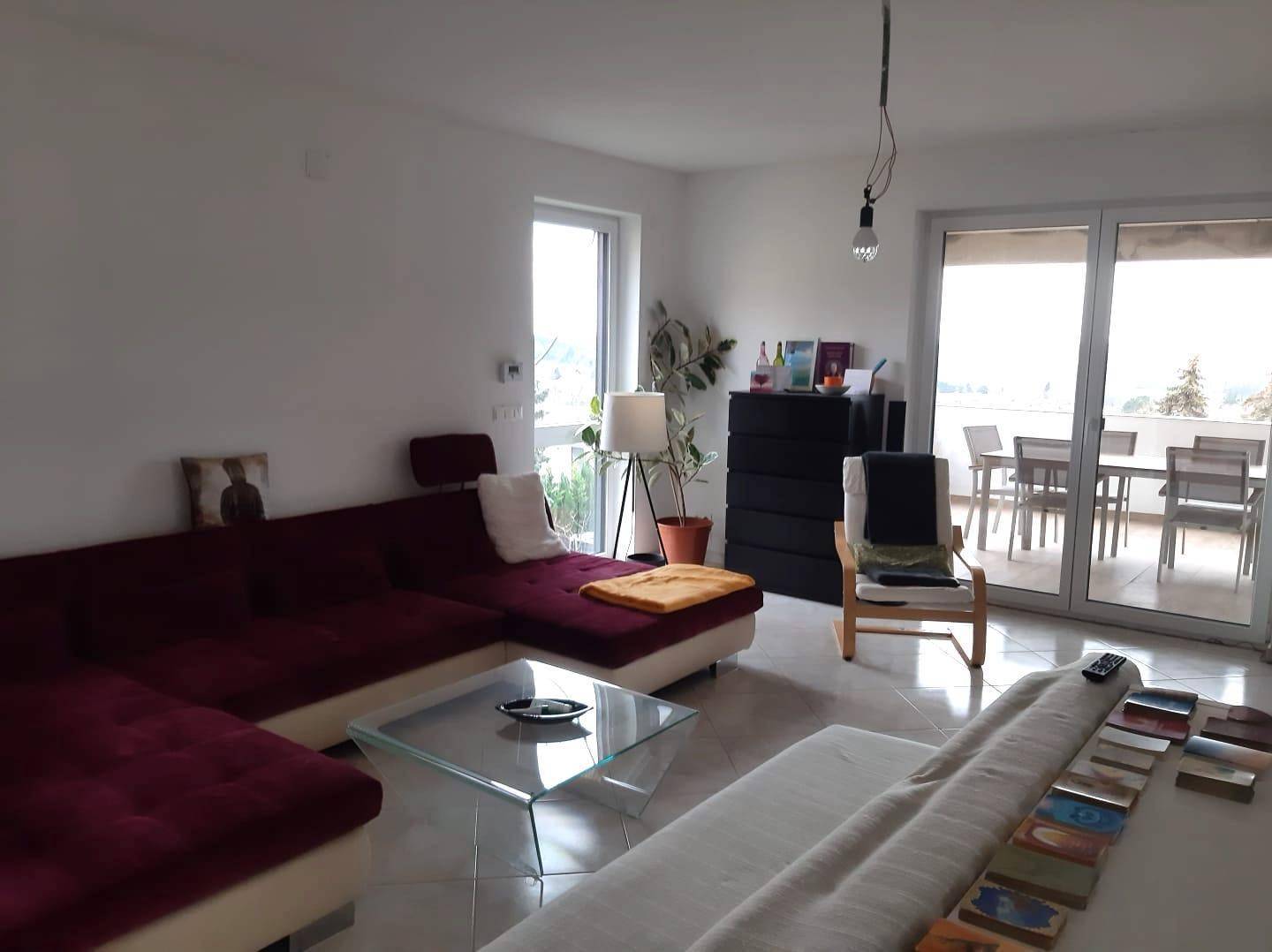 Gemütliches Wohnzimmer mit großem Sofa, Fliesenboden und Zugang zu einer Terrasse oder Balkon.
