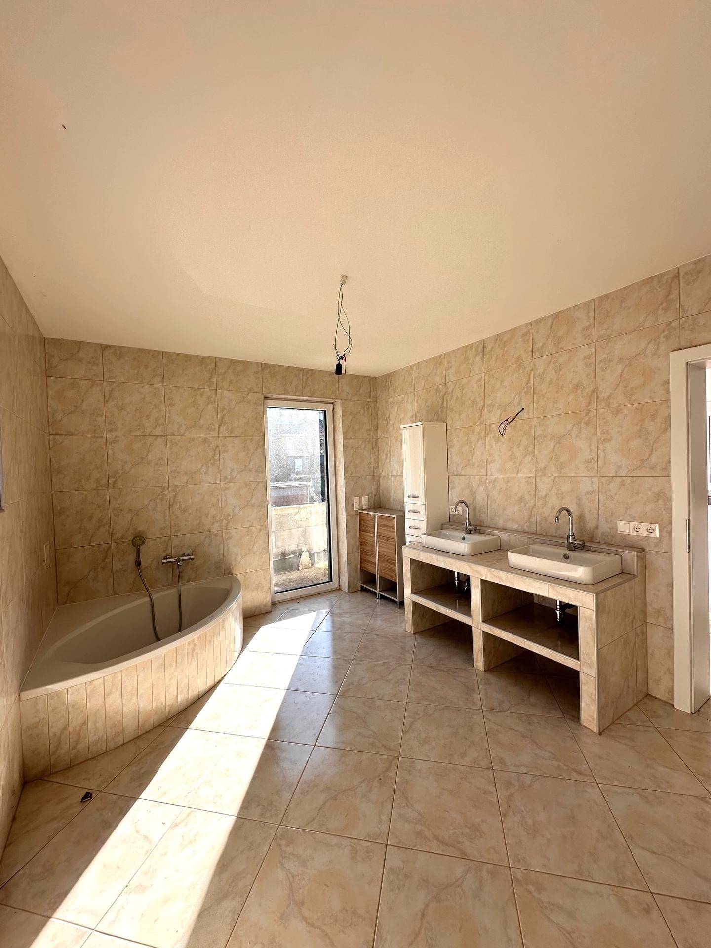 Geräumiges Badezimmer mit Eckbadewanne, Doppelwaschbecken und Fliesen an Wänden und Boden.