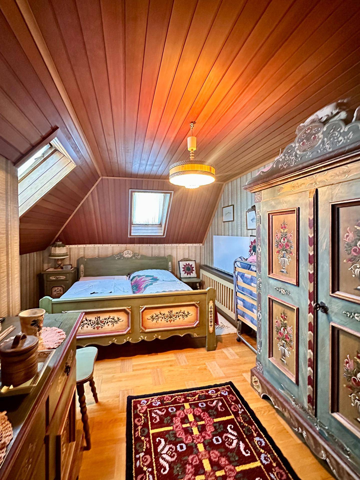 Gemütliches Schlafzimmer im Dachgeschoss mit Holztäfelung, traditionellen Möbeln und Dachfenstern.