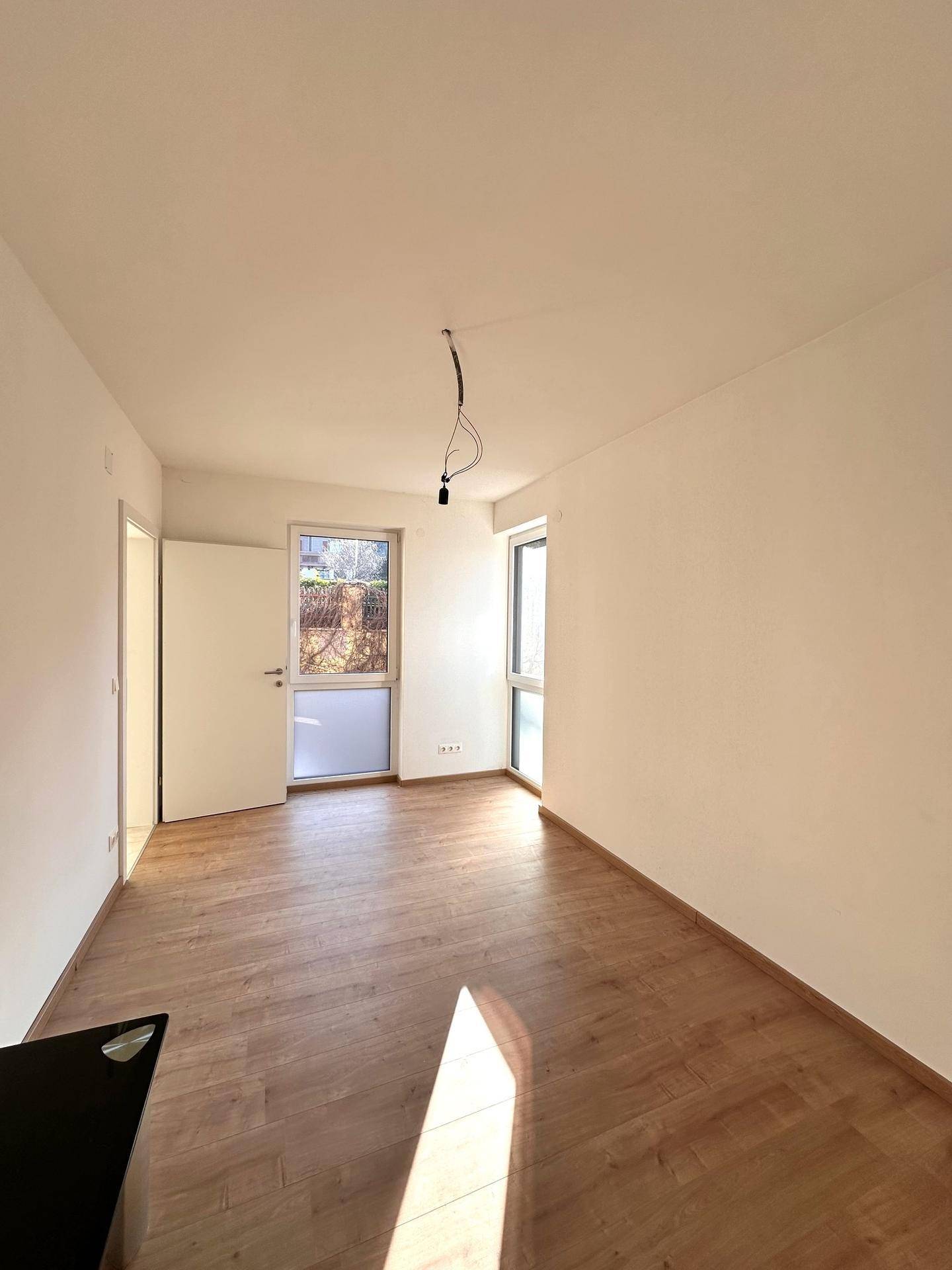 Helles Schlafzimmer mit Holzparkettboden und zwei Fenstern, die viel Tageslicht hereinlassen.
