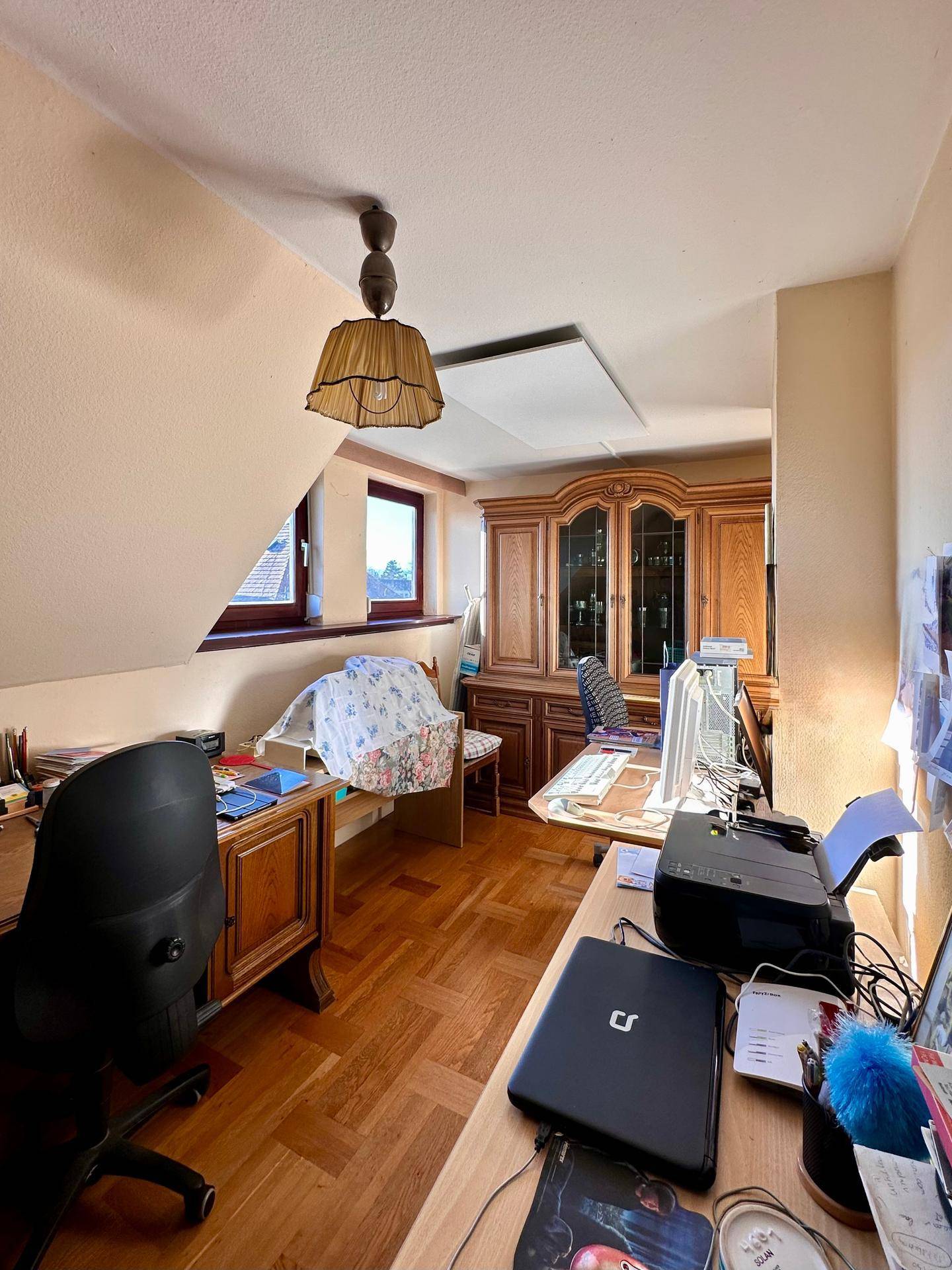 Helles Arbeitszimmer im Dachgeschoss mit Holzmöbeln, Parkettboden und Dachschrägen.