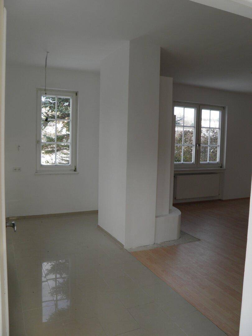 Übergangsbereich mit Fliesen- und Holzboden, einem Pfeiler und Fenstern mit Tageslicht.