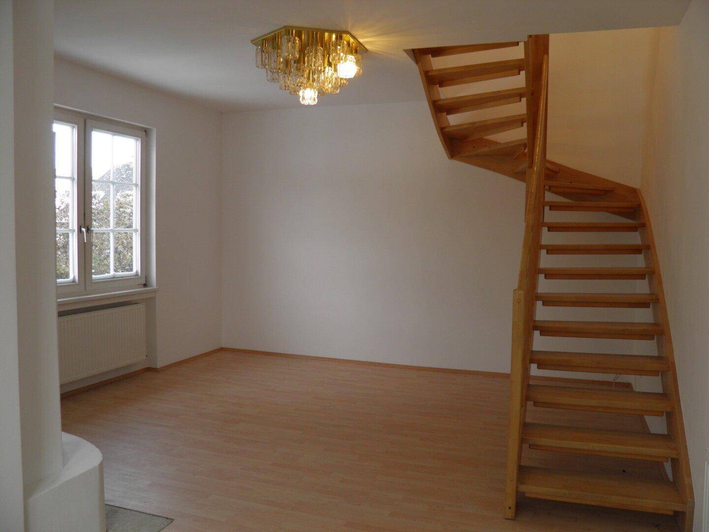 Heller Wohnbereich mit Holzboden, eleganter Holztreppe und einem dekorativen Kronleuchter.
