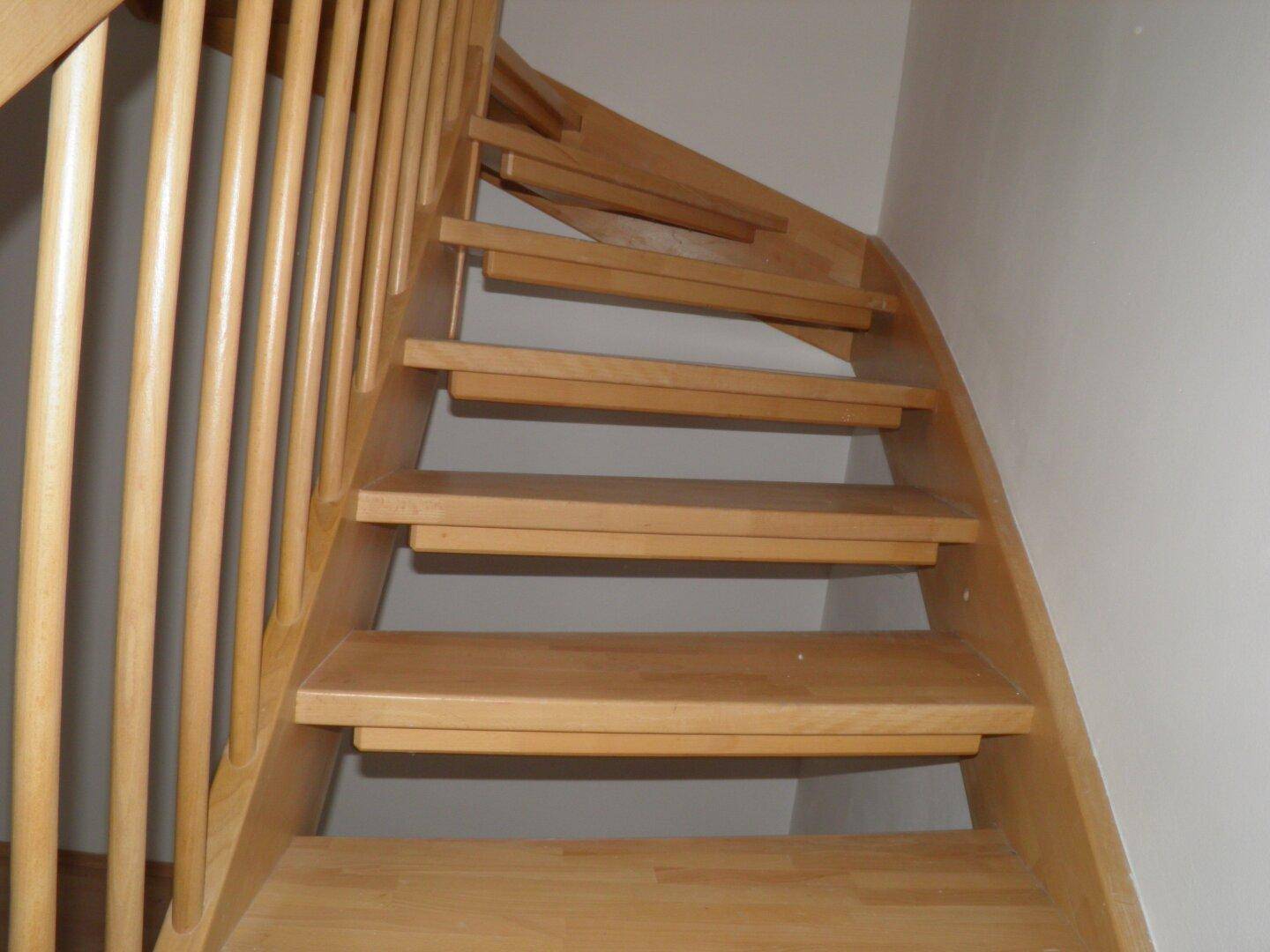 Detailansicht einer hellen Holztreppe mit Holzgeländer, die in die obere Etage führt.