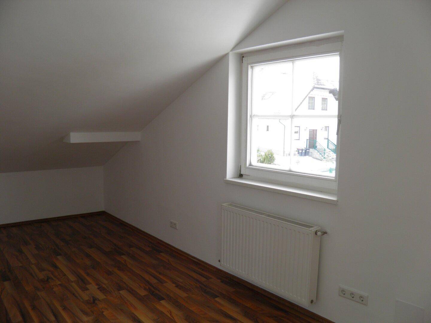 Gemütliches Schlafzimmer mit Holzboden, Heizkörper und Dachschräge, bietet einen ruhigen Ausblick.