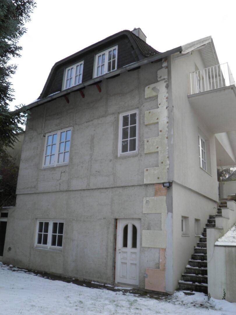 Historisches Gebäude mit Mansarddach, kleinem Balkon und Außentreppe, umgeben von winterlicher Landschaft.