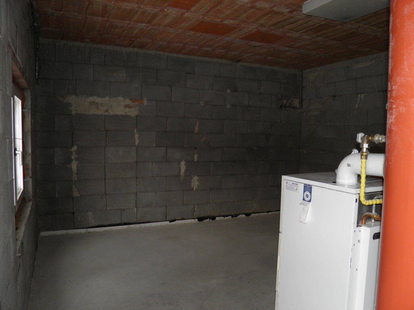 Unfertiger Kellerraum mit Betonsteinwänden und Heizungsanlage, ideal als Lager- oder Technikraum.