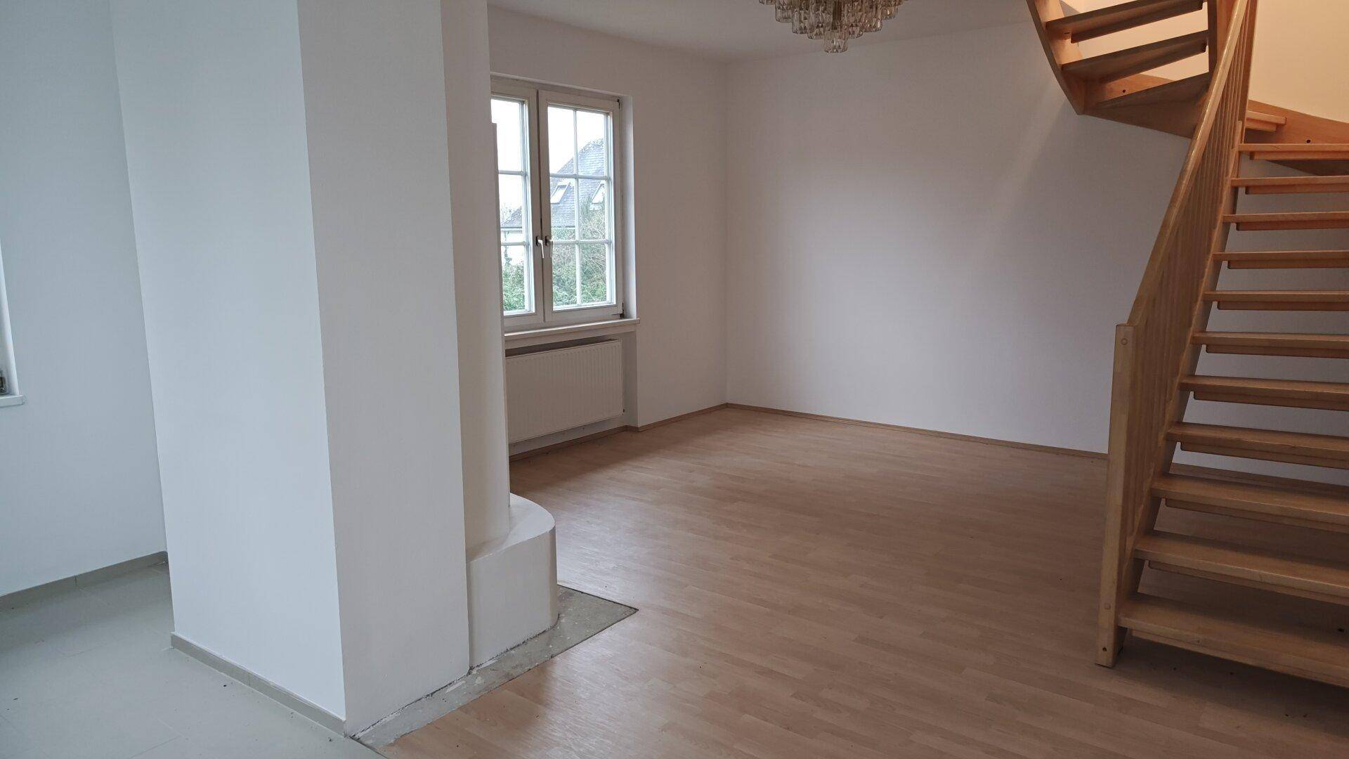 Wohnbereich mit hellem Holzboden und einer geschwungenen Holztreppe, die in die obere Etage führt.