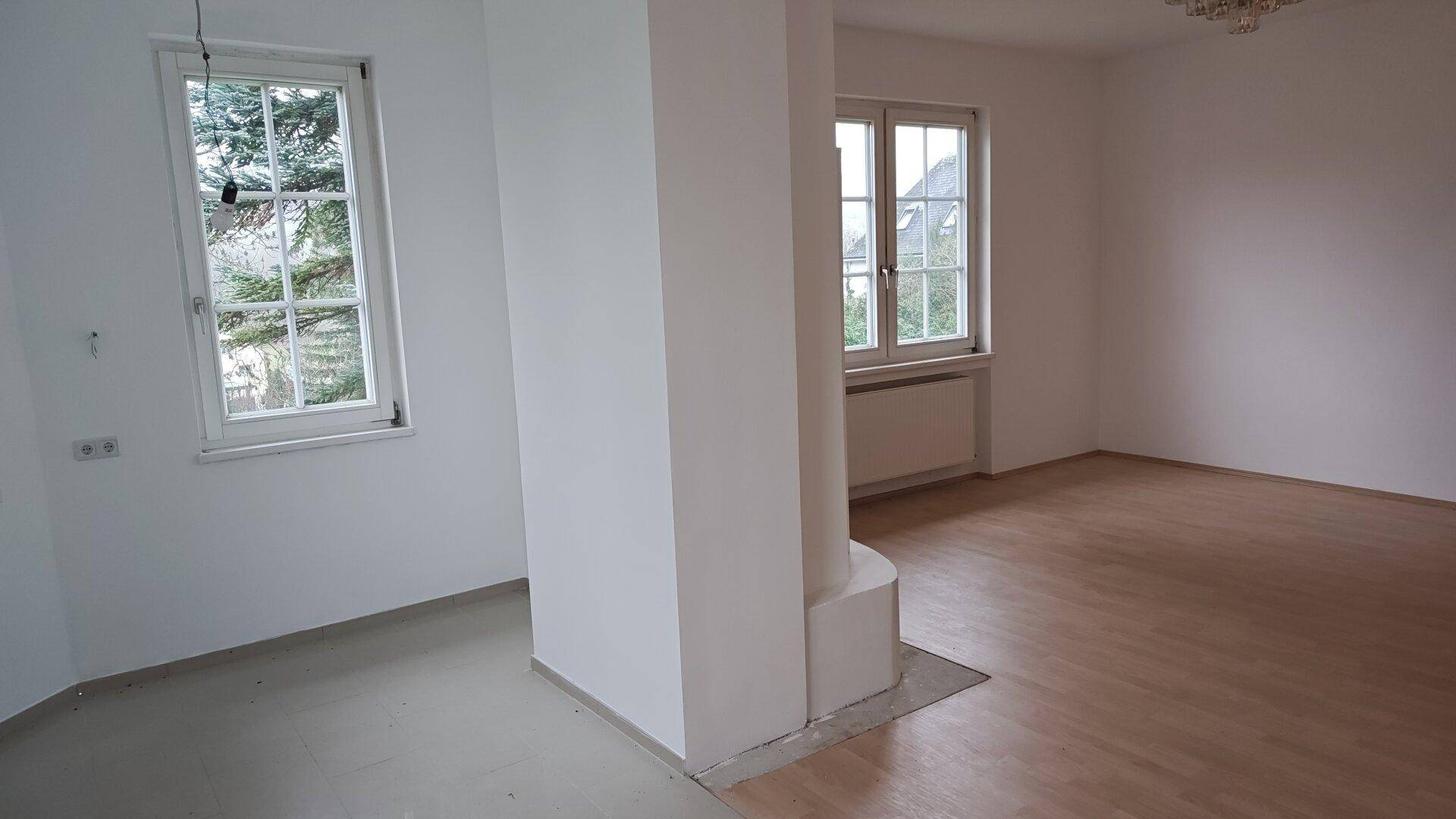 Heller Wohnbereich mit Holzboden, einem zentralen Pfeiler und Fenstern mit Ausblick.