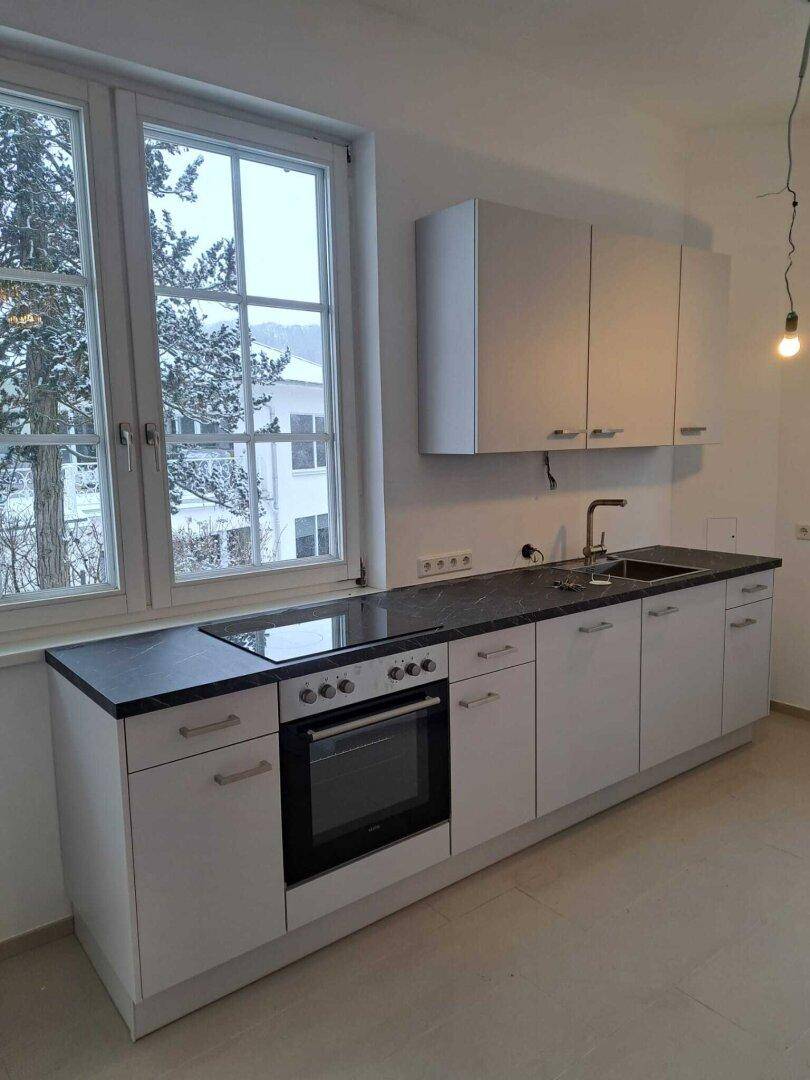 Helle Küche mit weißer Einbauküche, dunkler Arbeitsplatte und Blick aus dem Fenster.