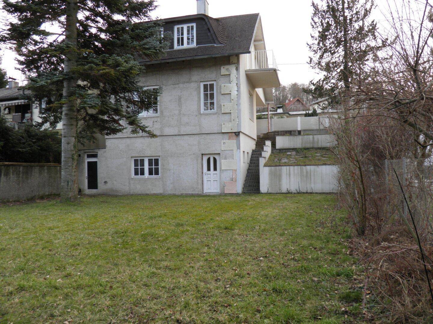 Ansicht des Einfamilienhauses von der Gartenseite mit Rasenfläche und altem Baumbestand im Winter.