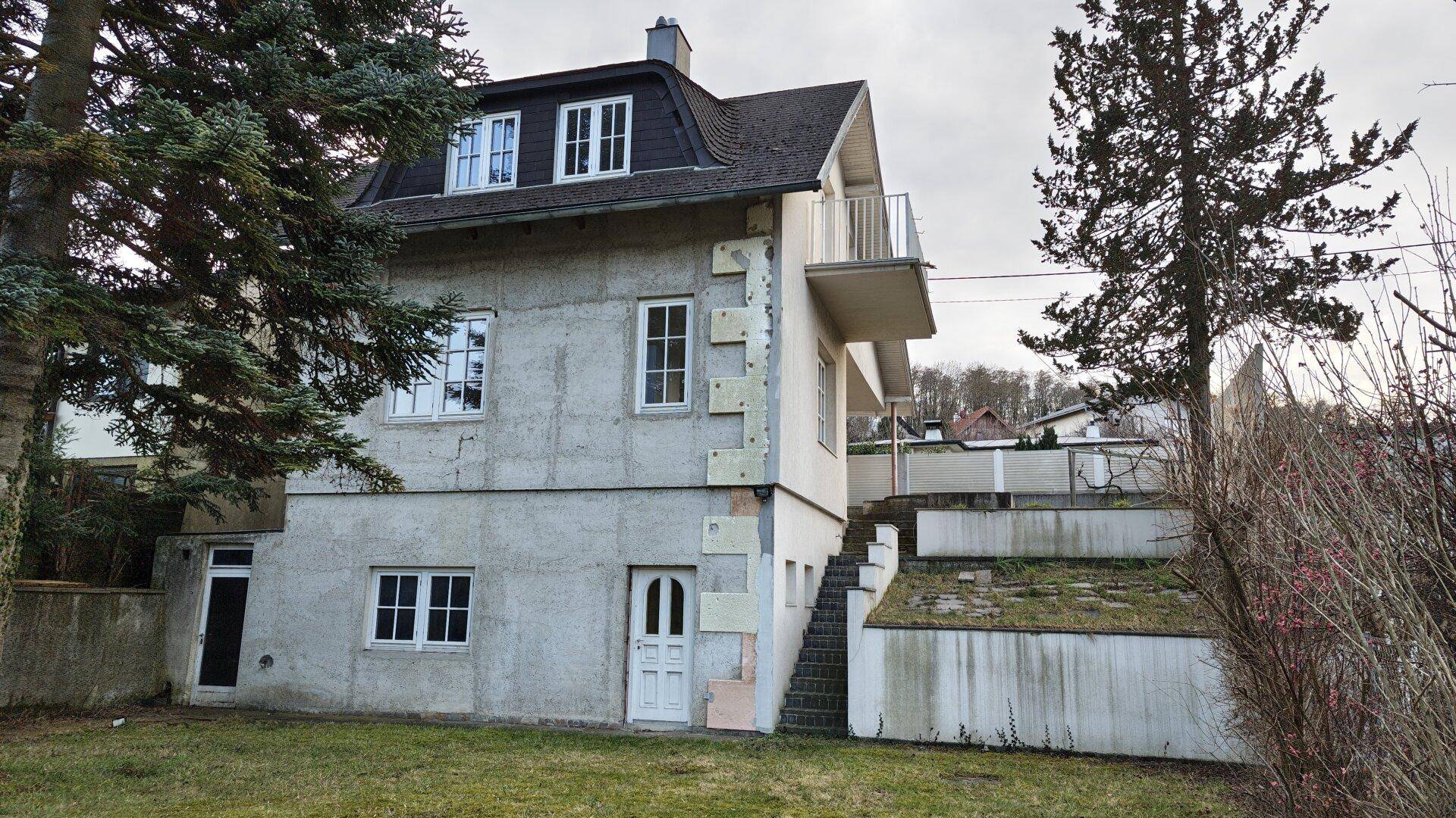 Außenansicht eines Einfamilienhauses mit Gartenbereich und Balkon, teilweise in Renovierung.