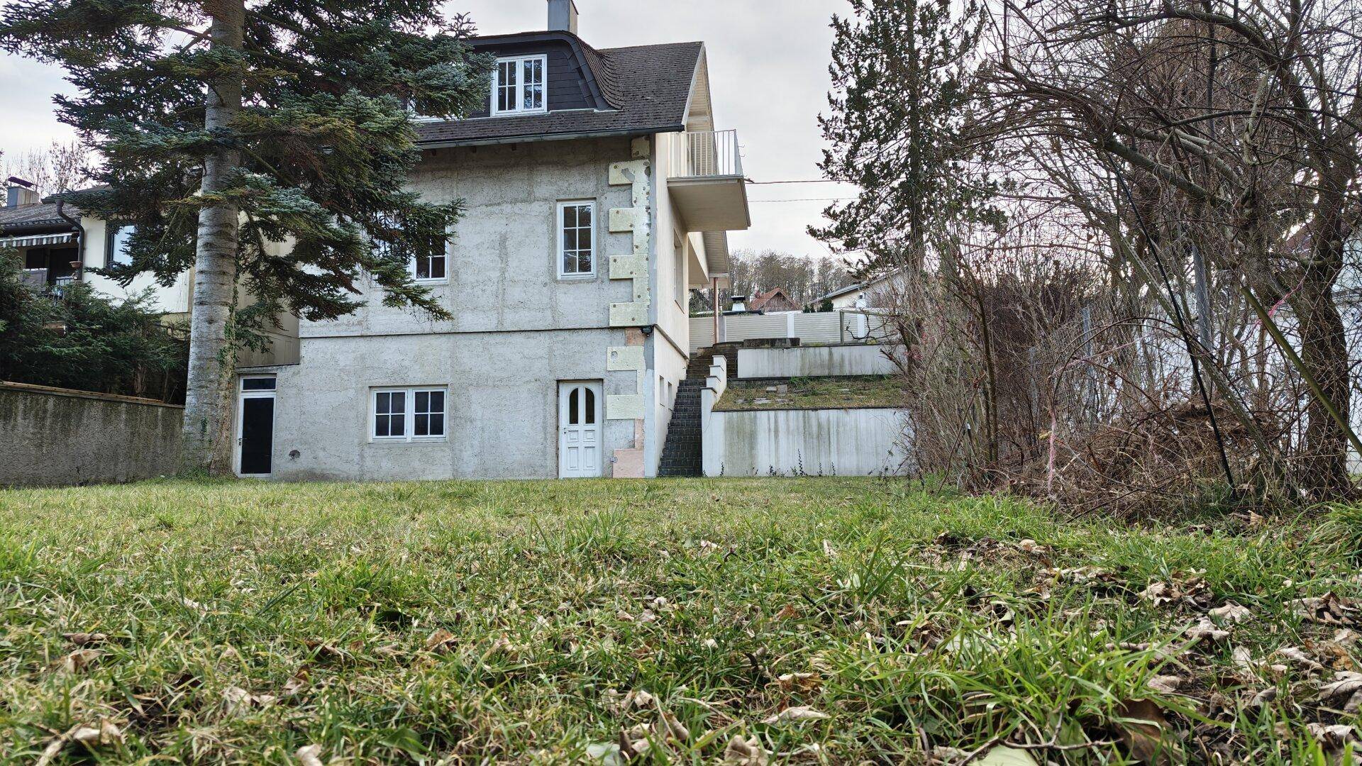 Blick vom Garten auf das Haus mit Rasenfläche und Bäumen im Vordergrund.