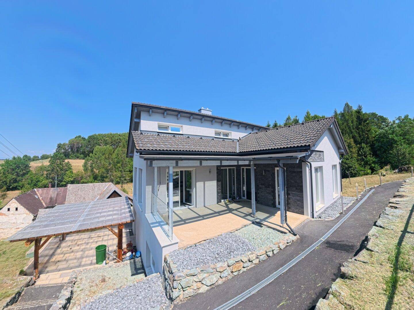 Modernes Einfamilienhaus mit grauen Dachziegeln und großzügiger Terrasse in ländlicher Umgebung.