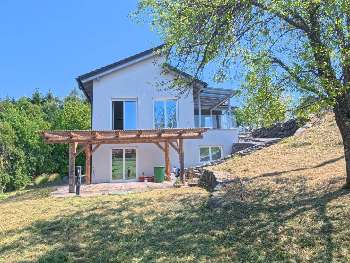 Rückansicht des Hauses mit überdachter Terrasse, Holzpergola und Blick in die Natur.