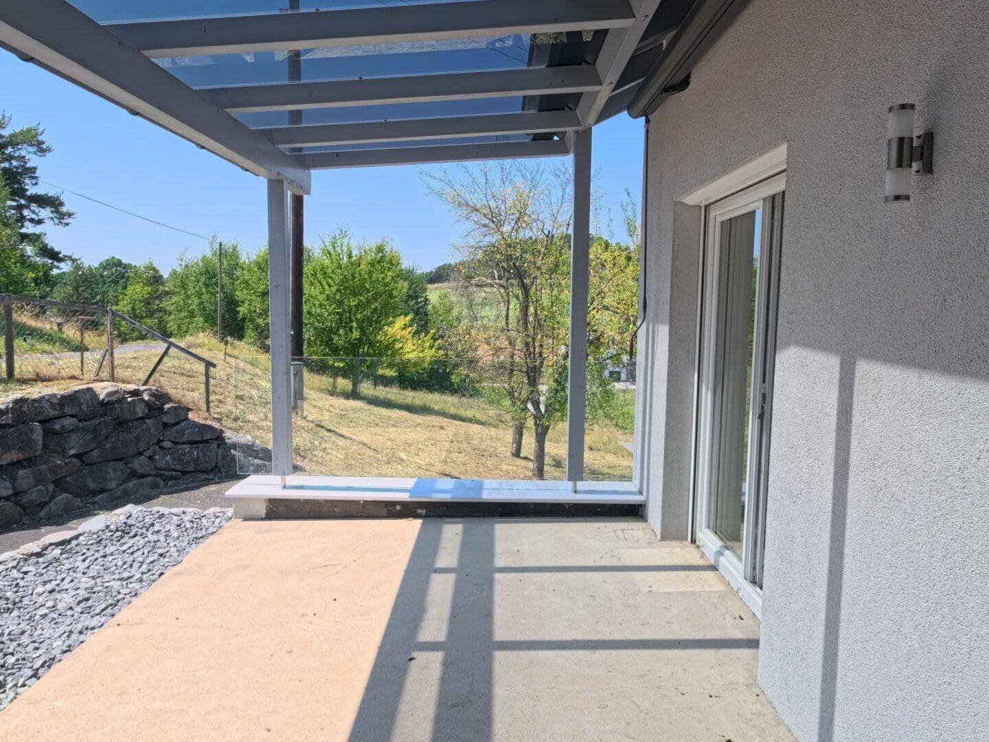 Überdachte Terrasse mit Glasgeländer und weitem Blick über die umliegende Landschaft.