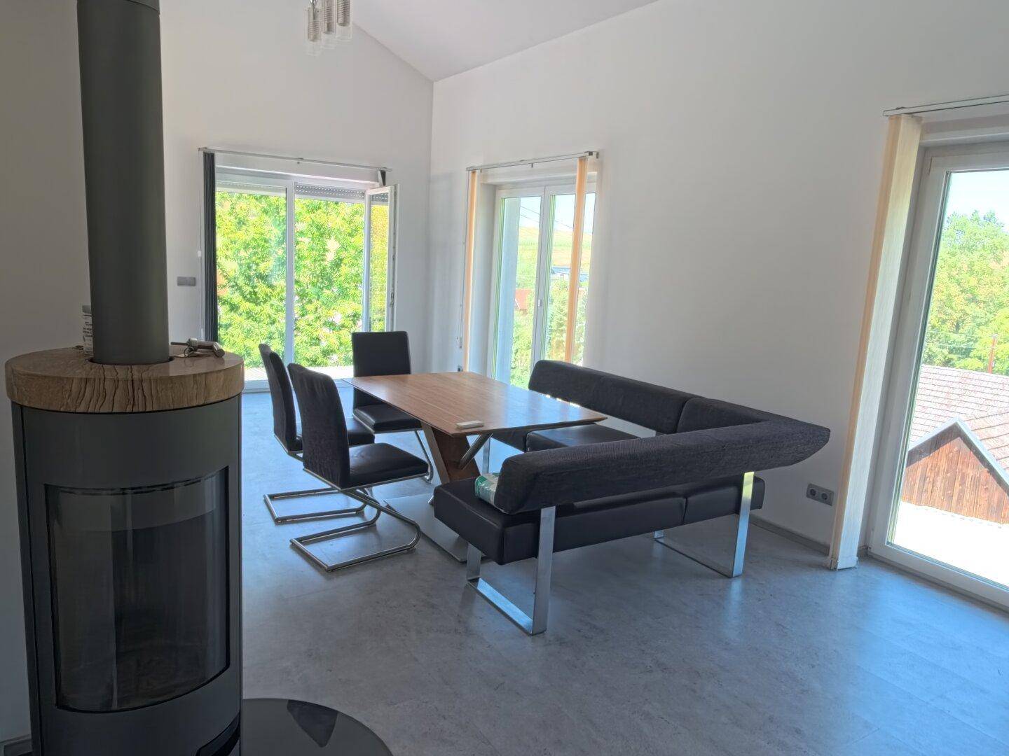 Heller Wohn-Essbereich mit modernem Kaminofen, großen Fenstern und Blick ins Grüne.