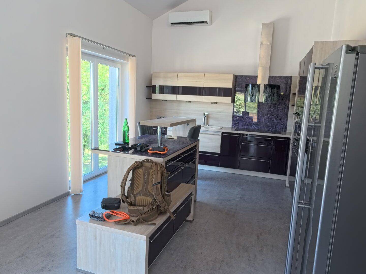 Moderne Küche mit Kücheninsel, dunklen Schränken und großem Kühlschrank, viel Tageslicht.