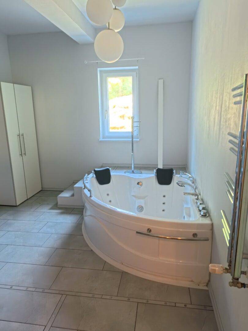 Geräumiges Badezimmer mit großer Eck-Whirlpool-Badewanne, Fenster und Handtuchheizkörper.