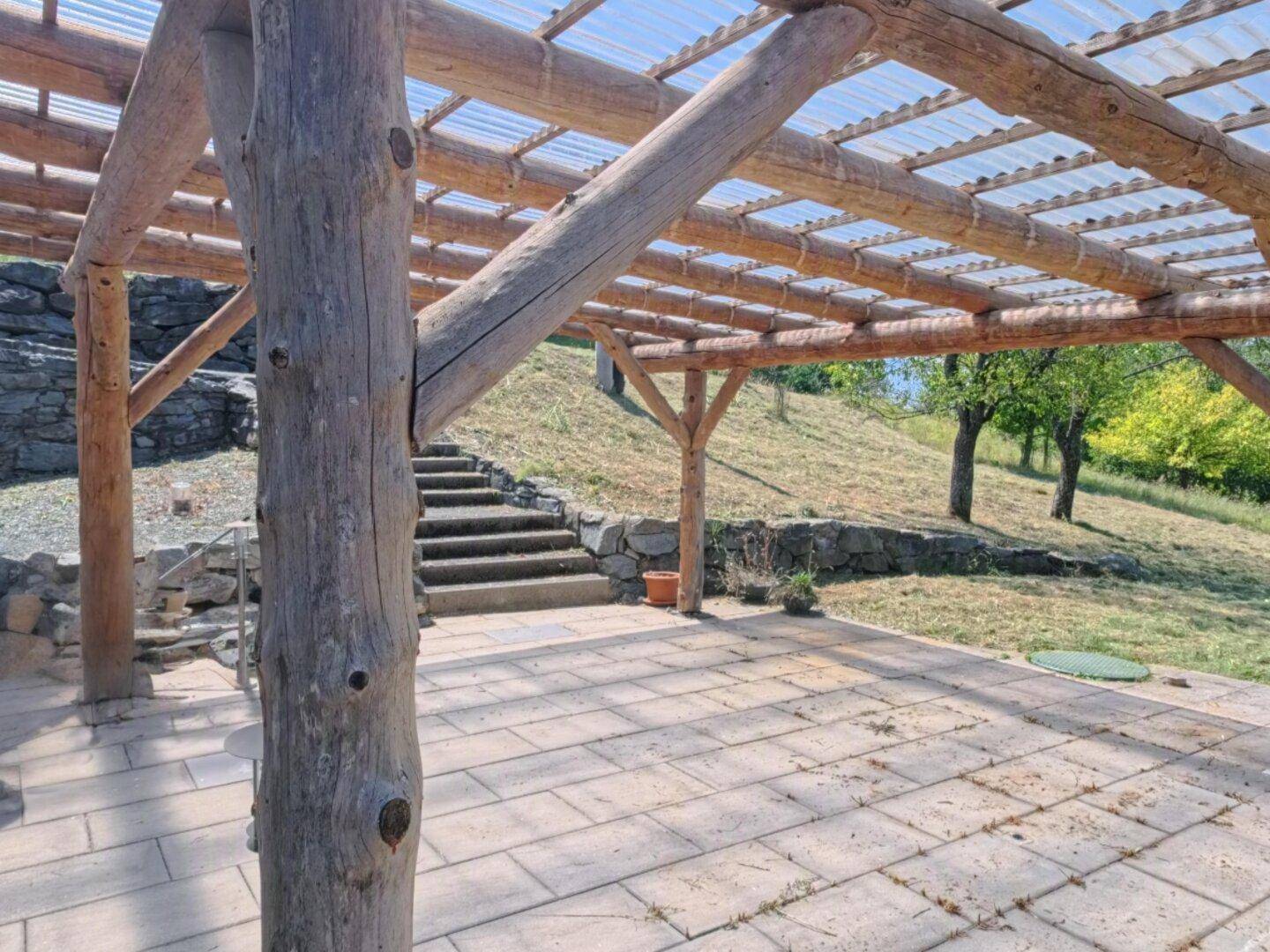 Gepflasterte Terrasse mit rustikaler Holzpergola und Treppe zum oberen Gartenbereich.