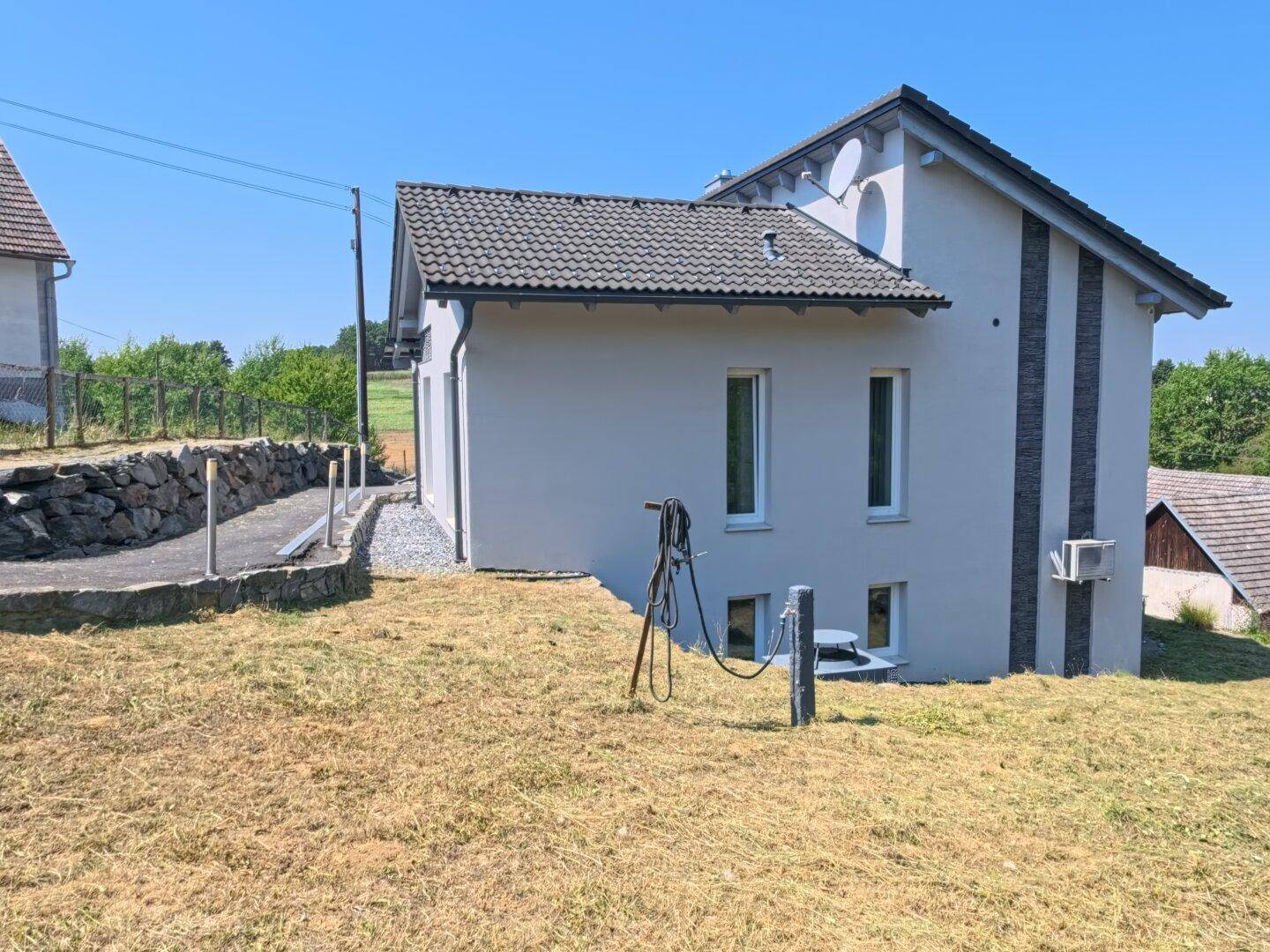 Seitenansicht des Hauses mit gepflegter Fassade und ländlicher Umgebung unter blauem Himmel.