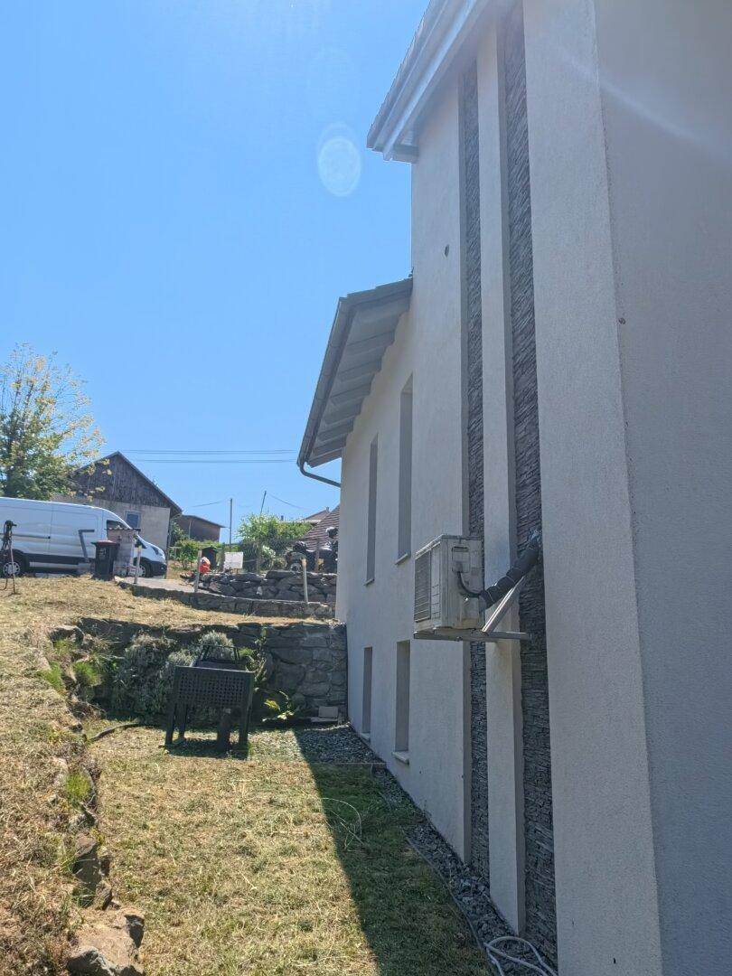 Seitenansicht des Hauses mit Klimaanlage und kleinem Gartenbereich mit Grill.