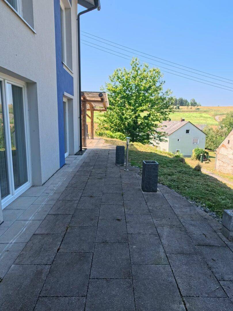 Gepflasterter Weg entlang des Hauses mit Blick auf die weite, grüne Landschaft.