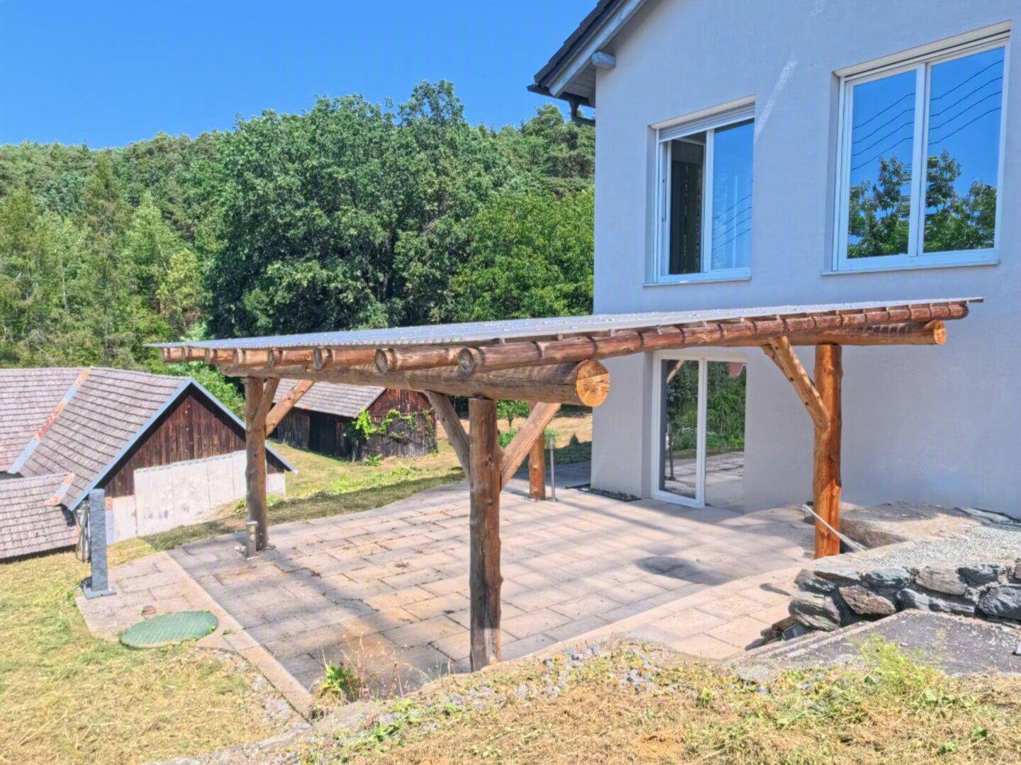 Rückseite des Hauses mit überdachter Terrasse und rustikaler Holzpergola für entspannte Stunden.
