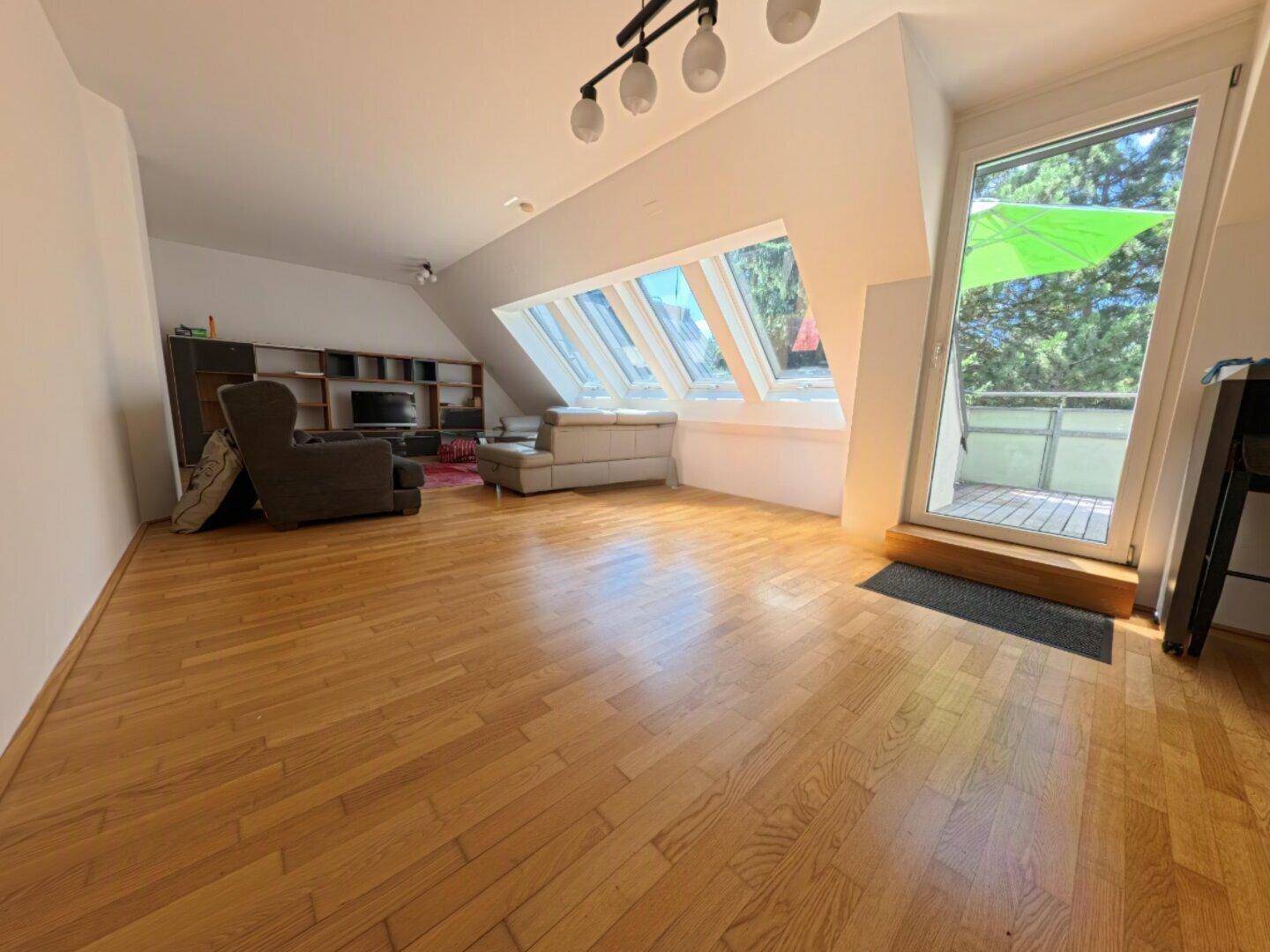 Helles Wohnzimmer mit Holzboden, Dachfenstern und Zugang zu einer Außenterrasse.
