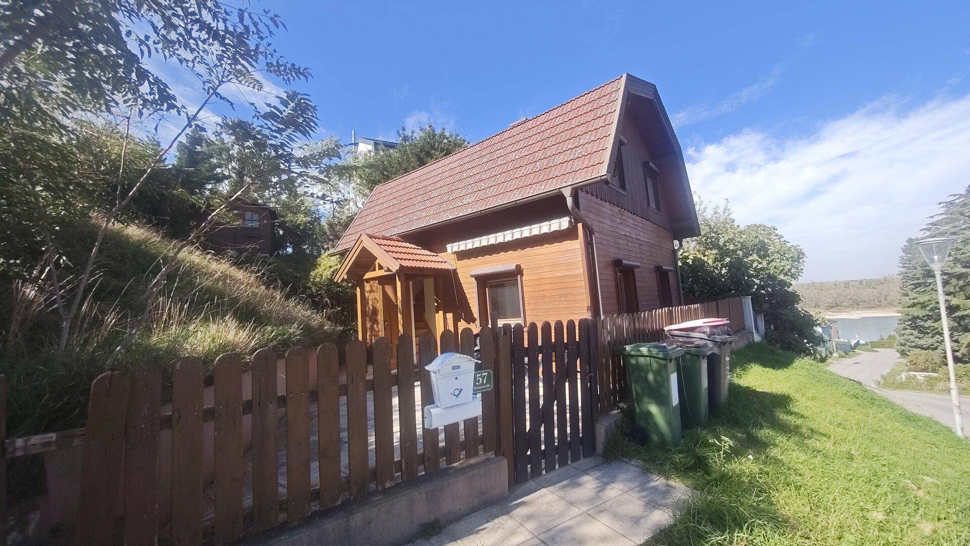 Freistehendes Holzhaus mit braunem Dach und Blick auf die umliegende Landschaft und ein Gewässer.