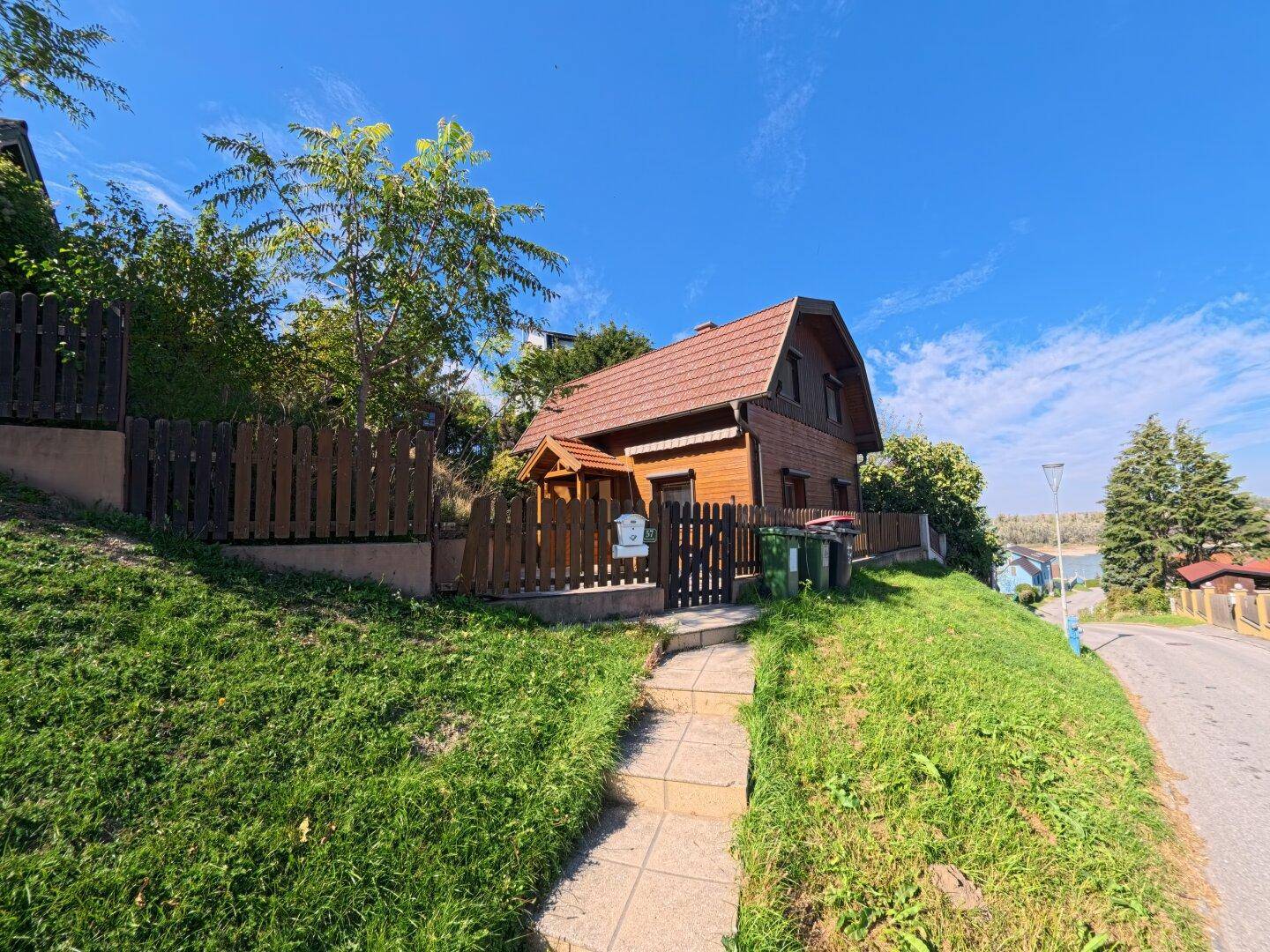 Das Holzhaus ist auf einem grünen Hang gelegen, mit einem gepflasterten Weg, der zum Eingang führt.