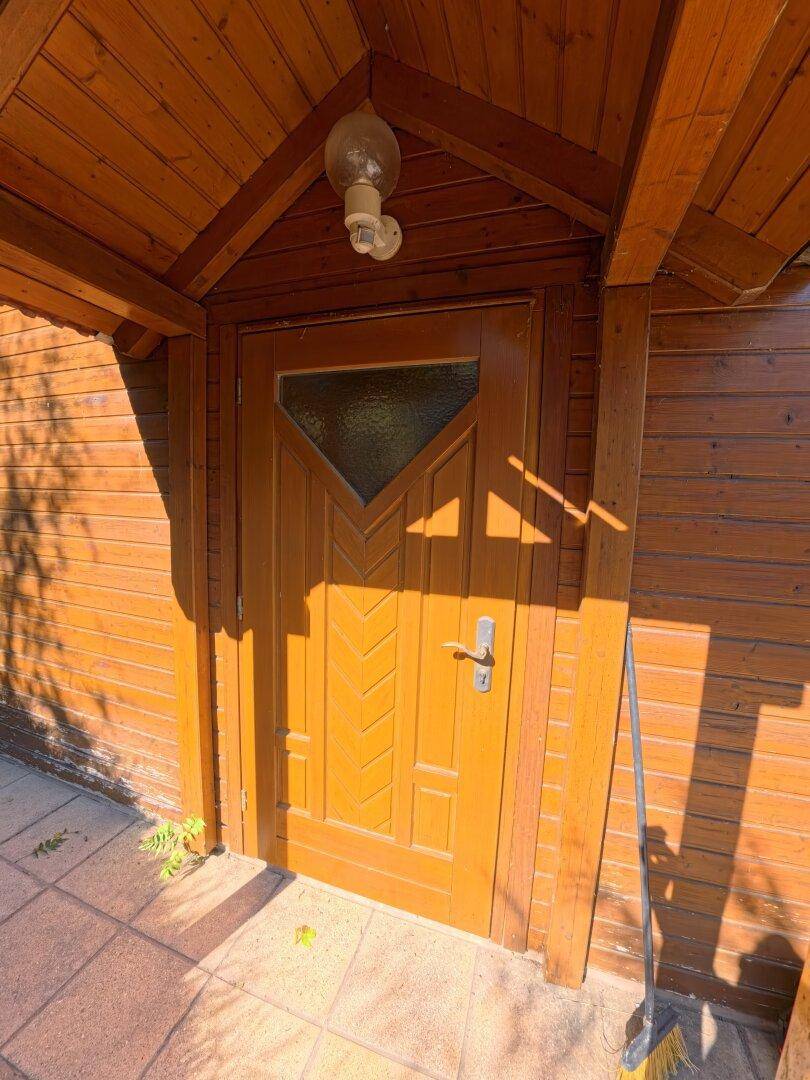 Detailaufnahme der hölzernen Eingangstür mit Glasausschnitt unter einem schützenden Vordach.