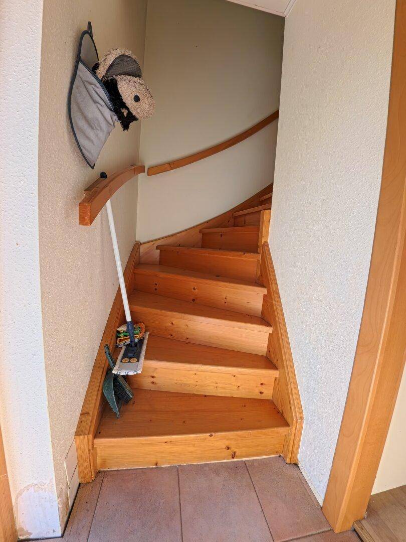 Hölzerne Treppe führt in das obere Stockwerk, mit Fliesenboden im unteren Bereich.