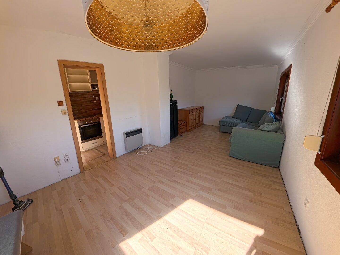 Helles Wohnzimmer mit Laminatboden, weiß gestrichenen Wänden und Zugang zur Küche.