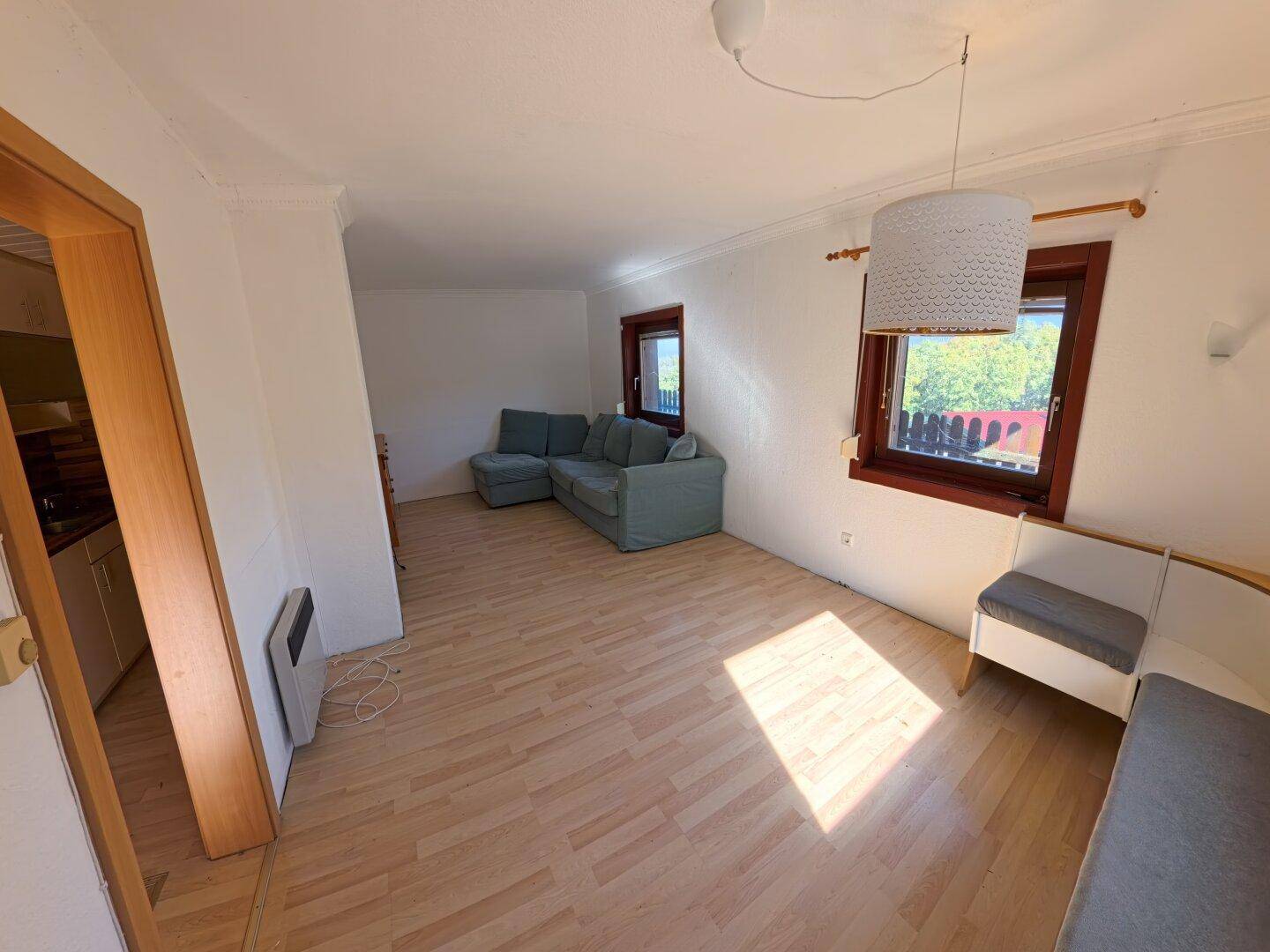 Gemütliches Wohnzimmer mit Ecksofa, Laminatboden und Fenstern, die viel Tageslicht hereinlassen.