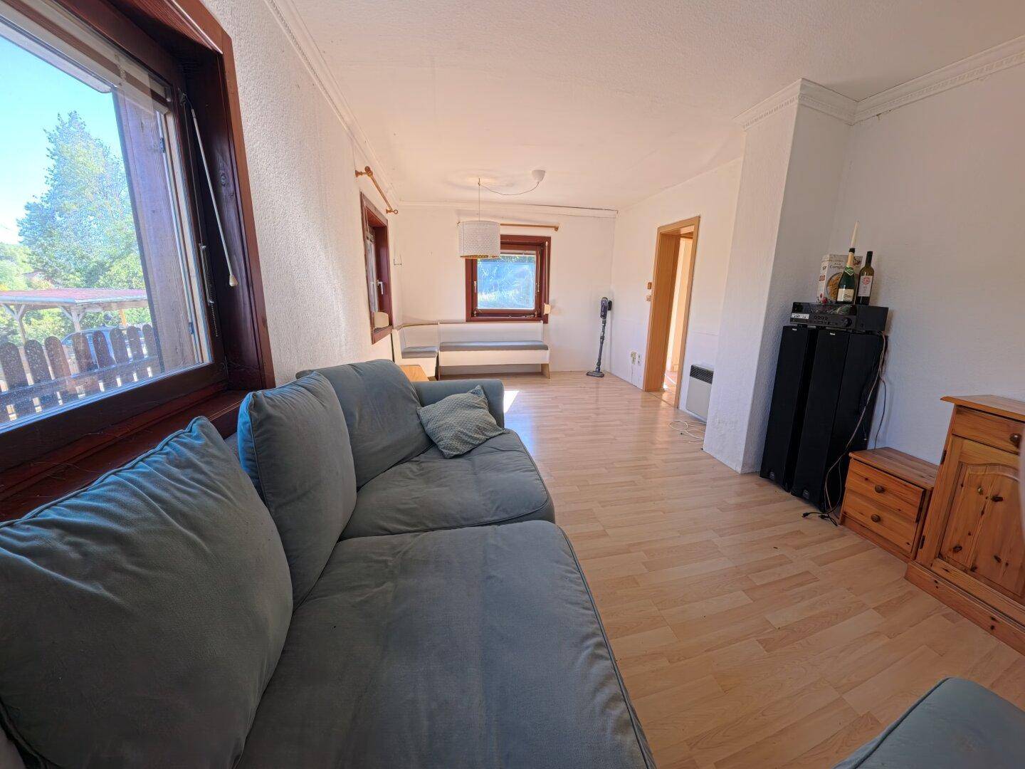 Wohnzimmer mit bequemer Couch und Fenstern, die einen angenehmen Blick ins Grüne bieten.