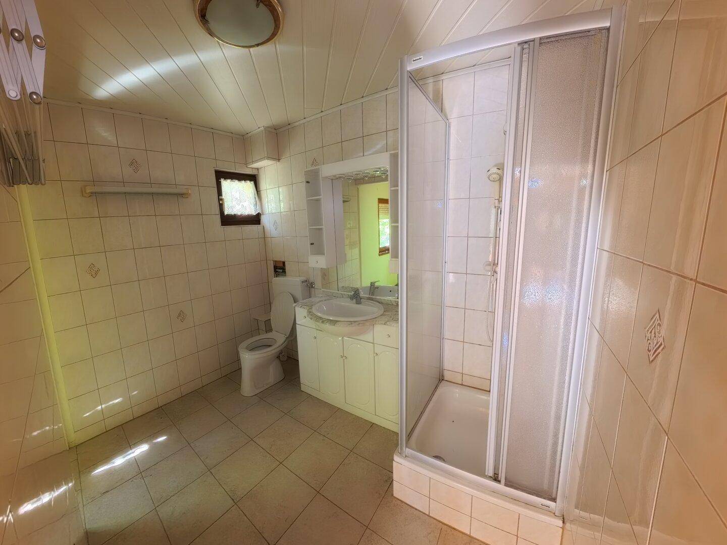 Gefliestes Badezimmer mit Duschkabine, Toilette und Einzelwaschbecken, in einem älteren Stil.