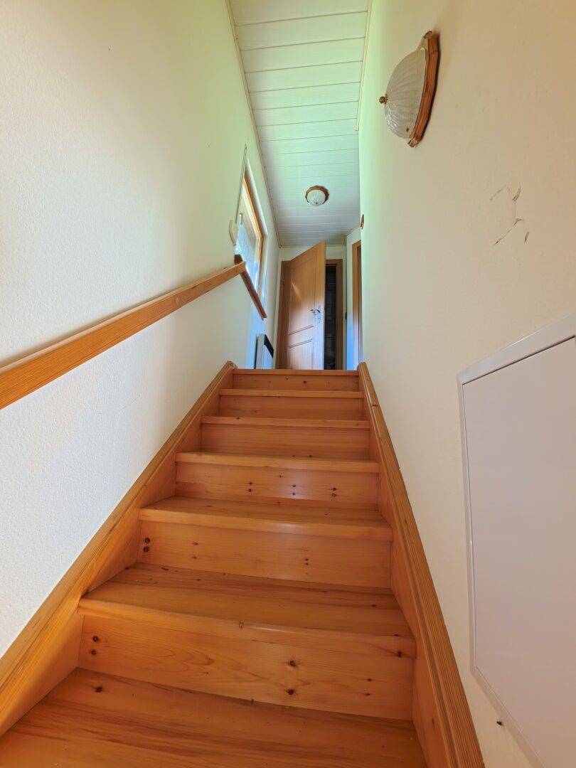 Blick die Holztreppe hinauf zu einem Flur im Obergeschoss mit einer Tür am Ende.