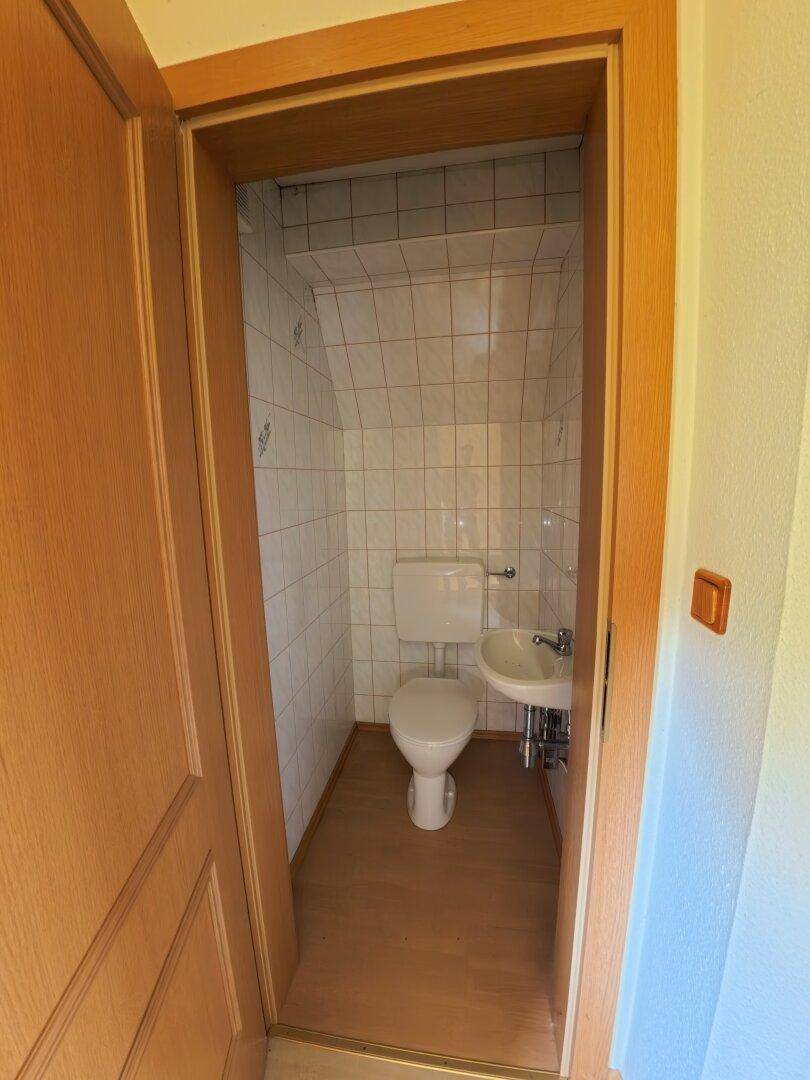 Kleines Gäste-WC mit gefliesten Wänden, Toilette und einem kompakten Eckwaschbecken.
