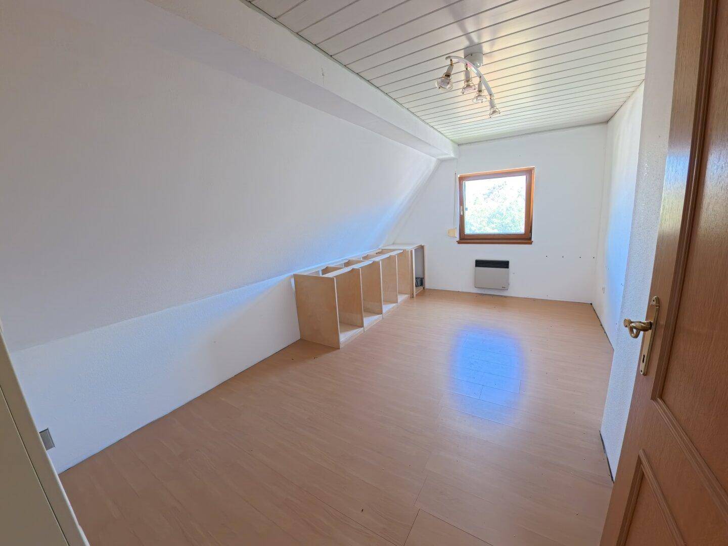Schlafzimmer im Dachgeschoss mit schrägen Wänden, Laminatboden und einem Fenster.