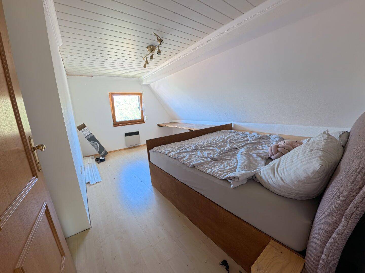 Dachgeschoss-Schlafzimmer mit Bettgestell, Laminatboden und schrägen Wänden, die Gemütlichkeit verleihen.