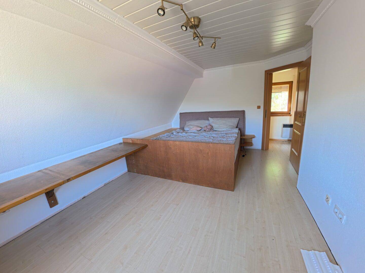 Helles Schlafzimmer im Dachgeschoss mit Holzbett, Laminatboden und einer langen Ablagefläche.