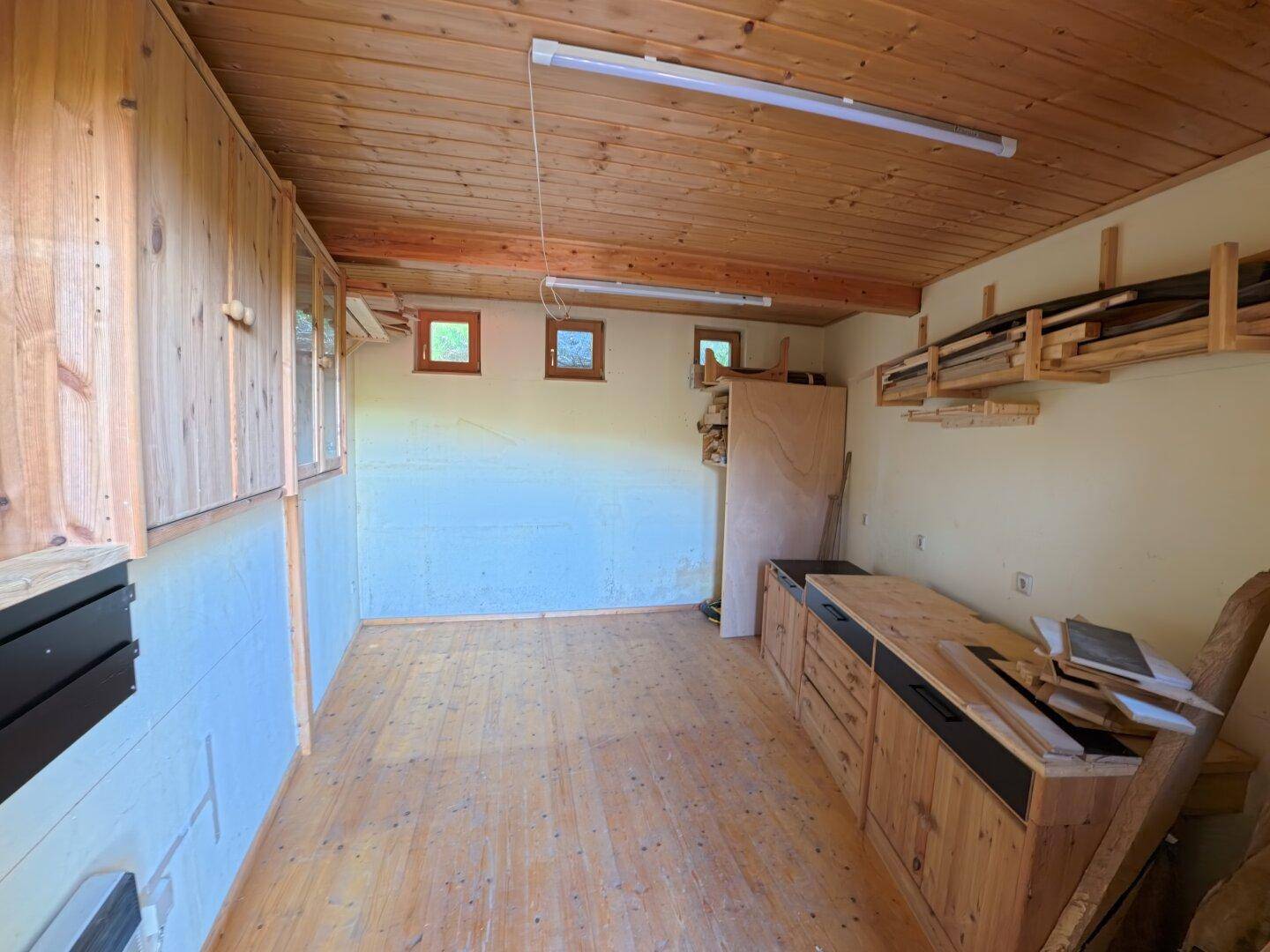 Geräumiger Holz-Werkstattraum mit Holzwänden, Decke und Arbeitsflächen, ideal für handwerkliche Tätigkeiten.