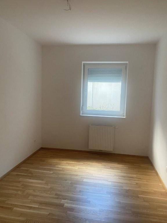 Leeres Zimmer mit Parkettboden, Heizkörper und Fenster mit Rollladen.