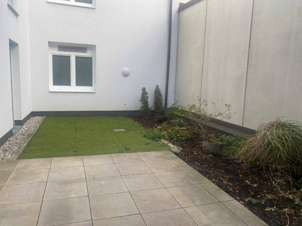 Kleine gepflasterte Terrasse mit Kunstrasenfläche und Bepflanzung im Hinterhof.