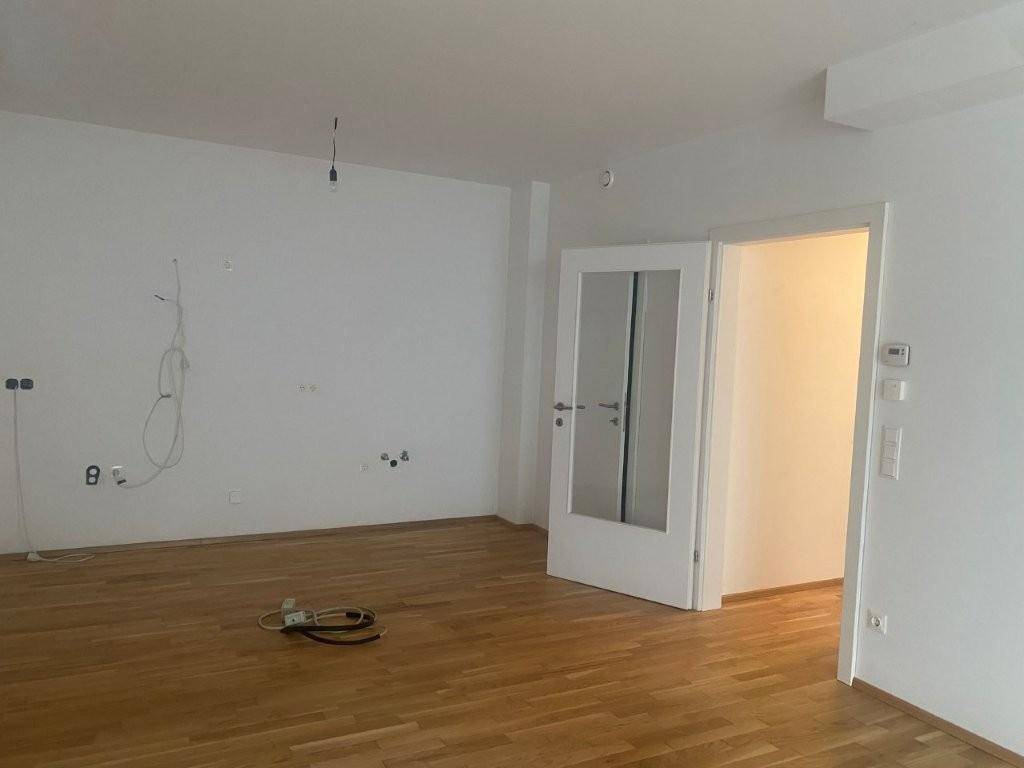 Geräumiger Raum mit Parkettboden, weißen Wänden und vorbereiteten Elektroinstallationen.